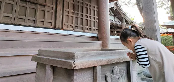 神社の前で手を合わせ願う少女の画像